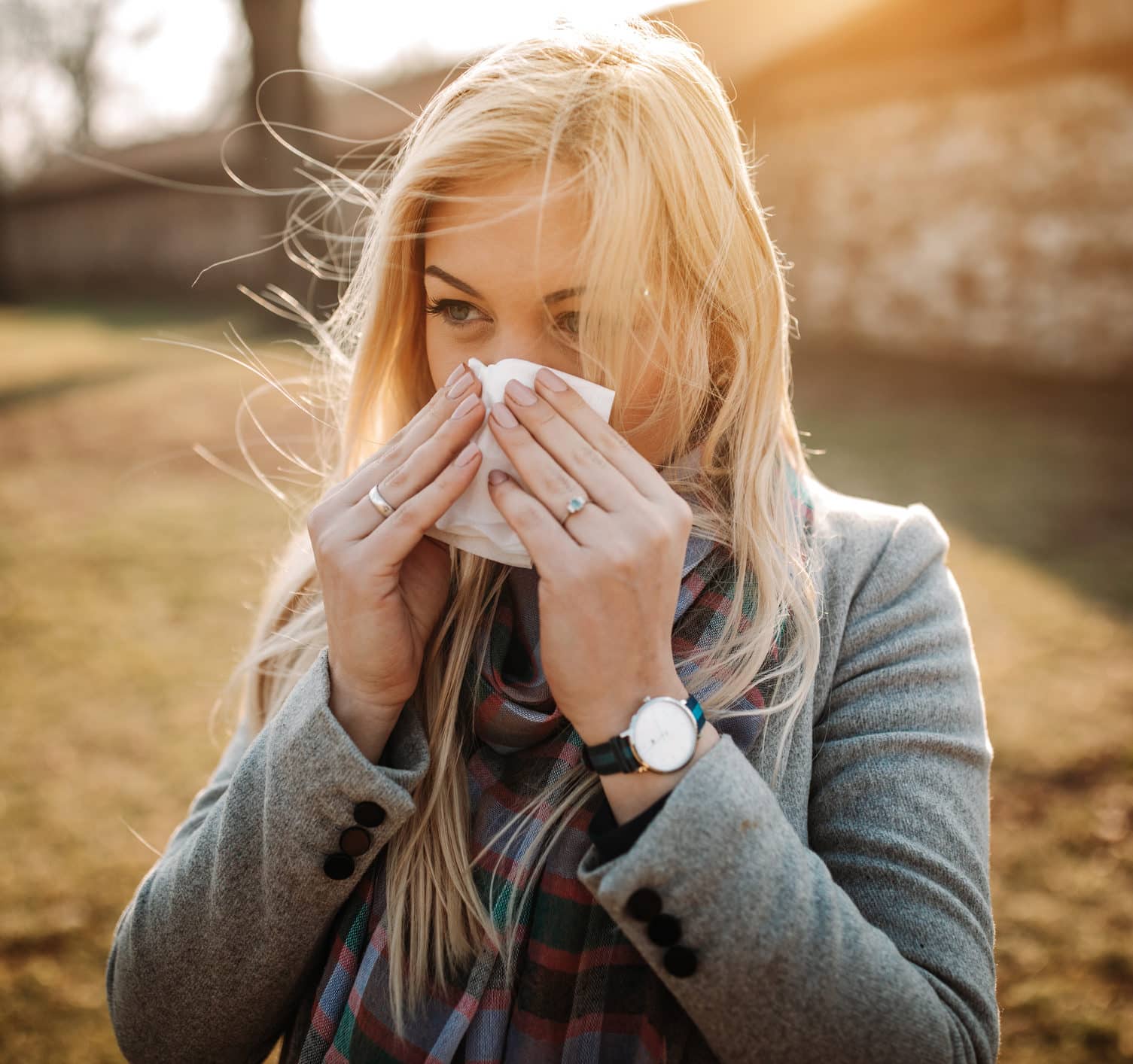 close up of young woman blowing her nose with a tissue outside